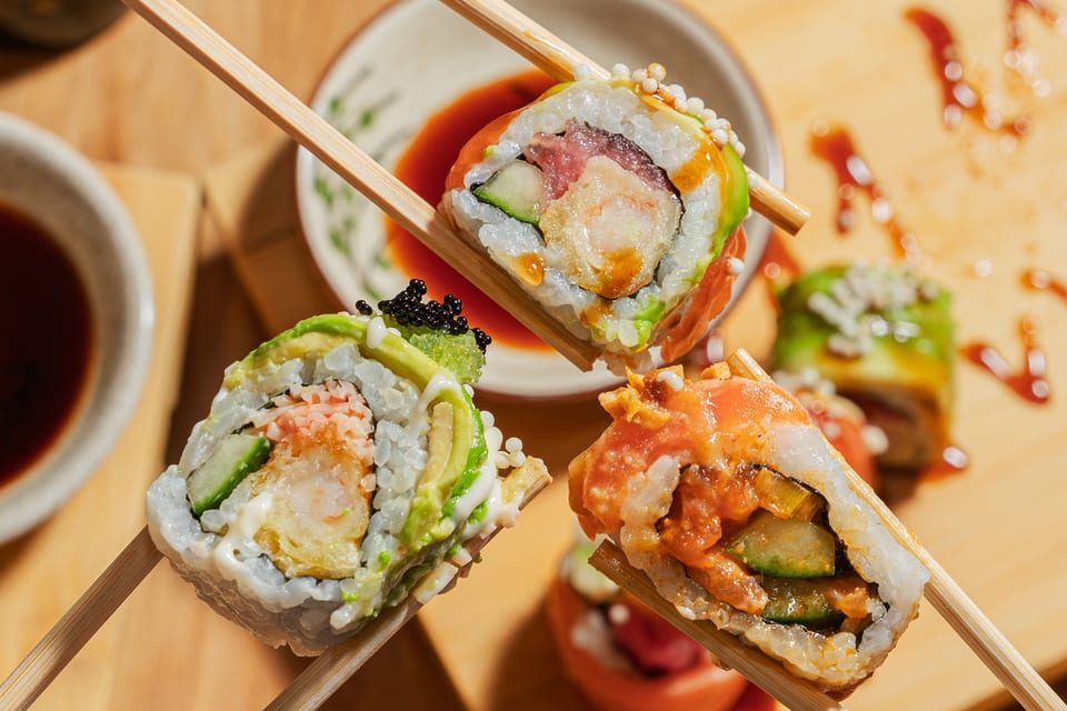 Three different sushi rolls, held by chopsticks, with dipping sauce in the background.