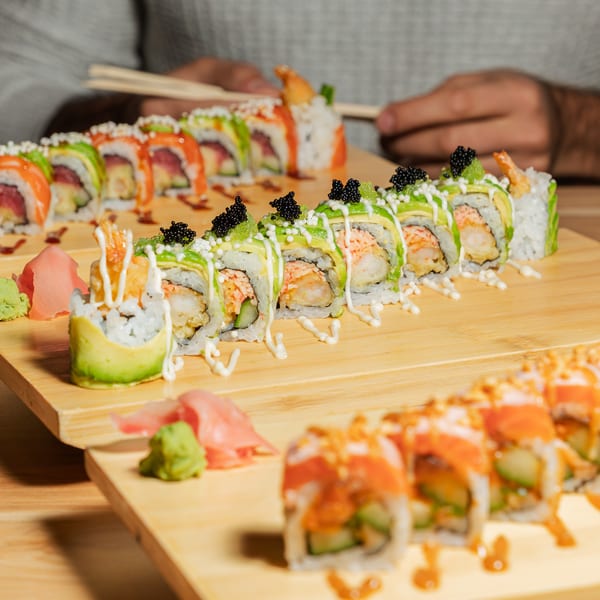 Three rows of sushi rolls with various toppings, wasabi, and ginger on wooden boards.