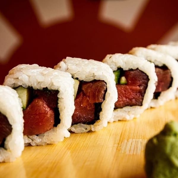 Row of fresh tuna and cucumber sushi rolls with wasabi and pickled ginger on a wooden board.