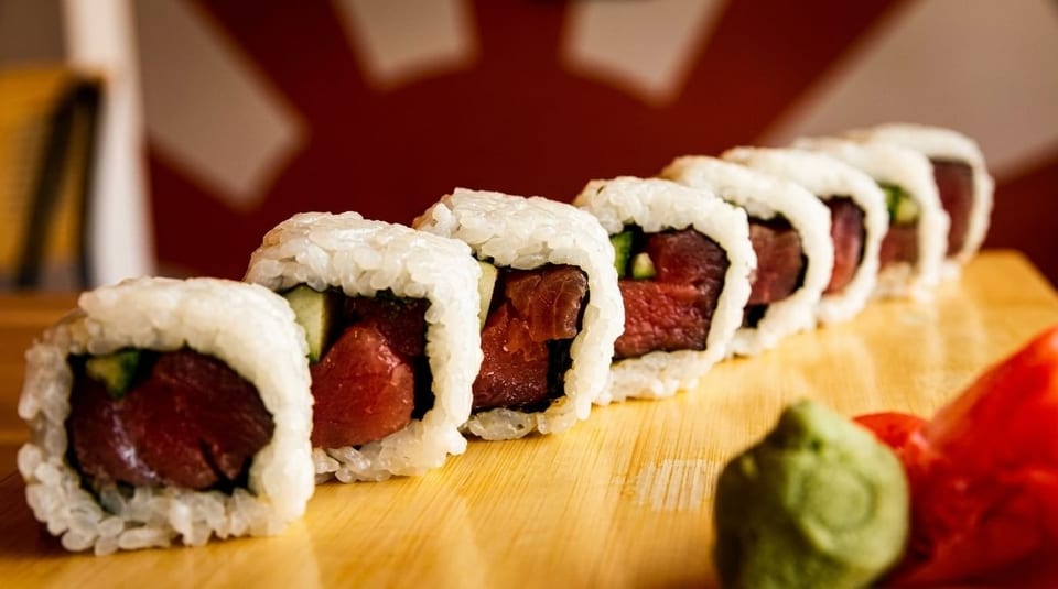 Row of fresh tuna and cucumber sushi rolls with wasabi and pickled ginger on a wooden board.